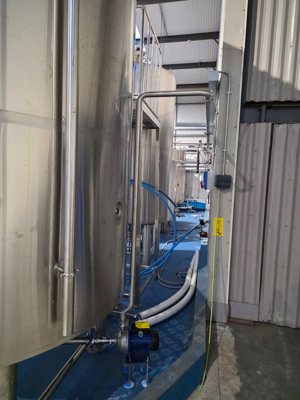 Stainless steel pipework and pump alongside a brewery vessel
