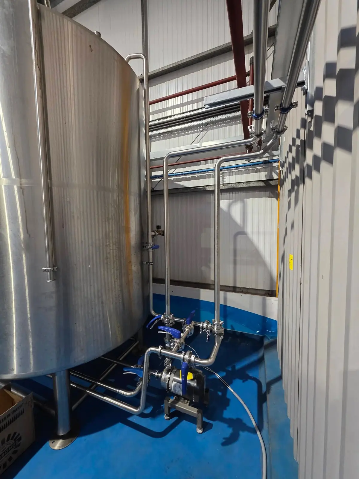 Pump and valve cluster with stainless steel pipework beside a brewery vessel