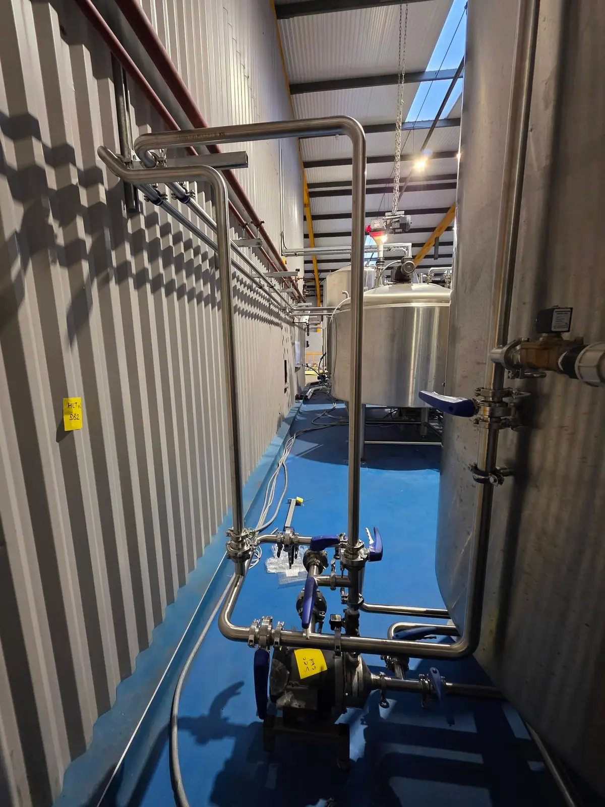 Stainless steel process pipework running along a brewery wall to a pump