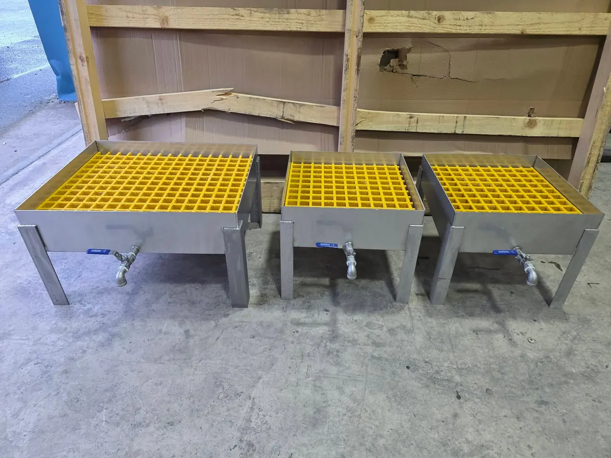 Three stainless steel drip trays with yellow grating and drain valves