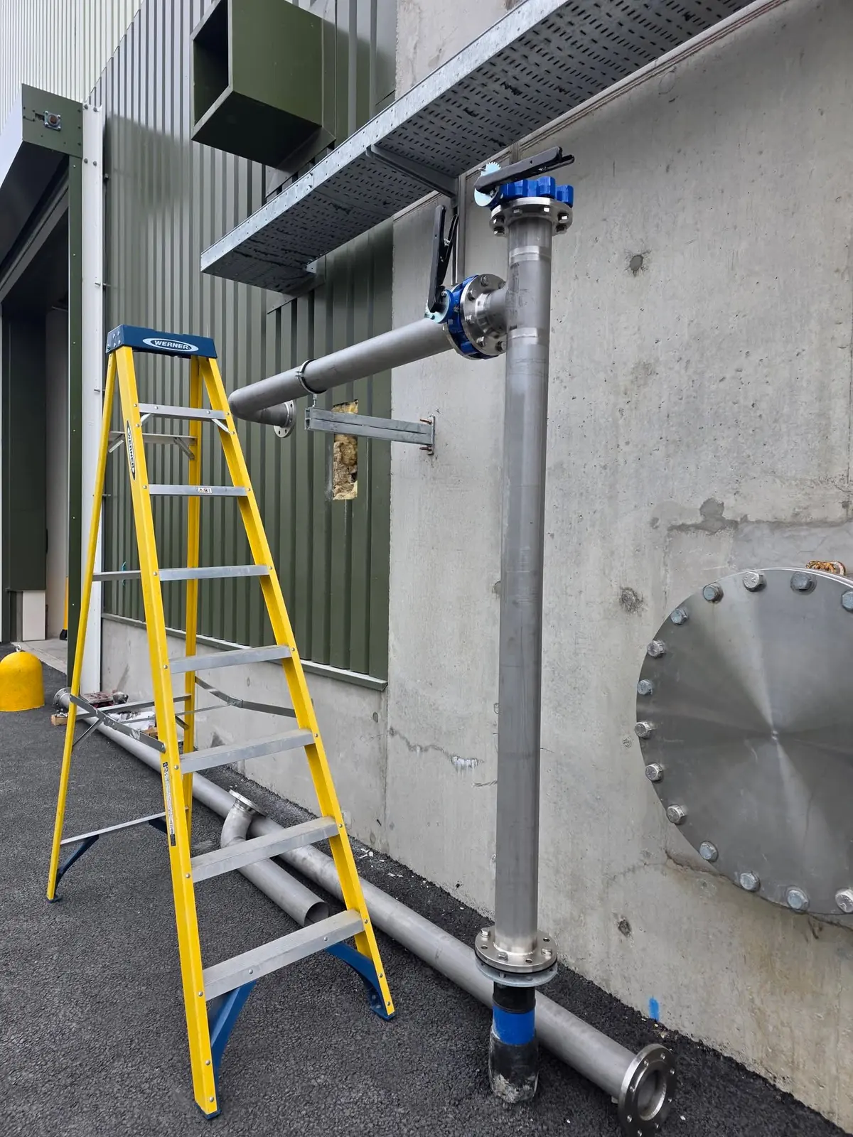 Stainless steel water line with a butterfly valve fixed to a concrete wall beside a ladder