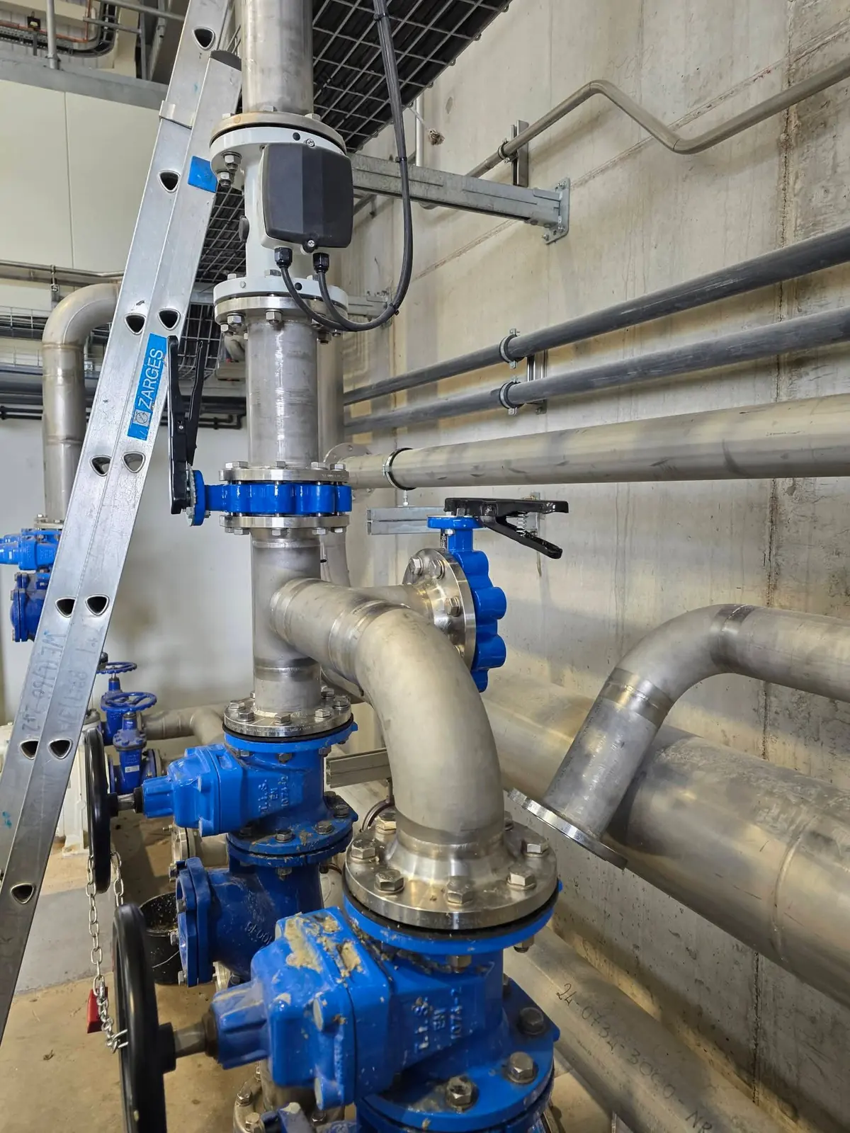 Stainless steel water pipework with blue valves and flanged joints inside a plant room