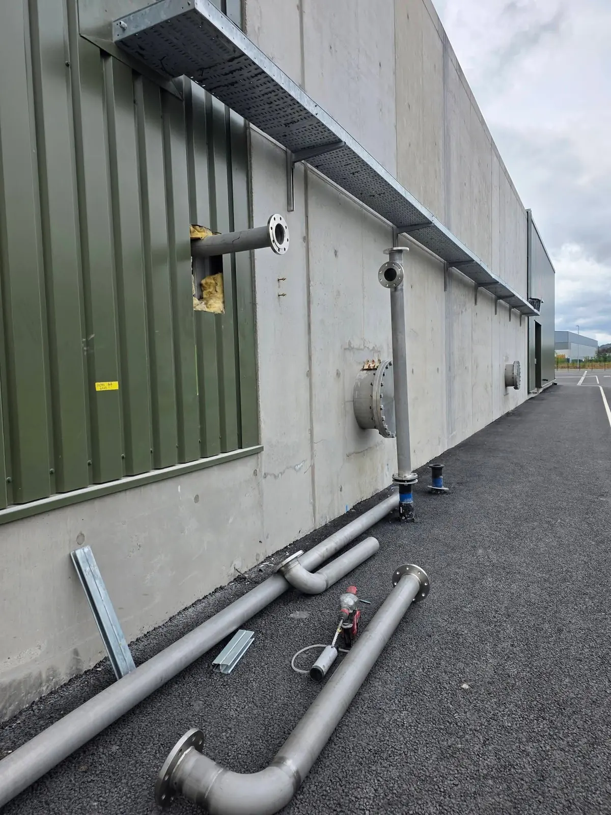 Stainless steel water line pipework with flanges laid out and fitted along an industrial building wall
